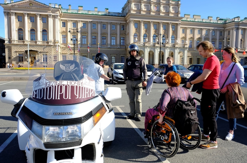 На фото: Большой белый трицикл на Синем мосту, Марина Козикова на коляске разговаривает с командой мотоциклистов и коллегами по проекту