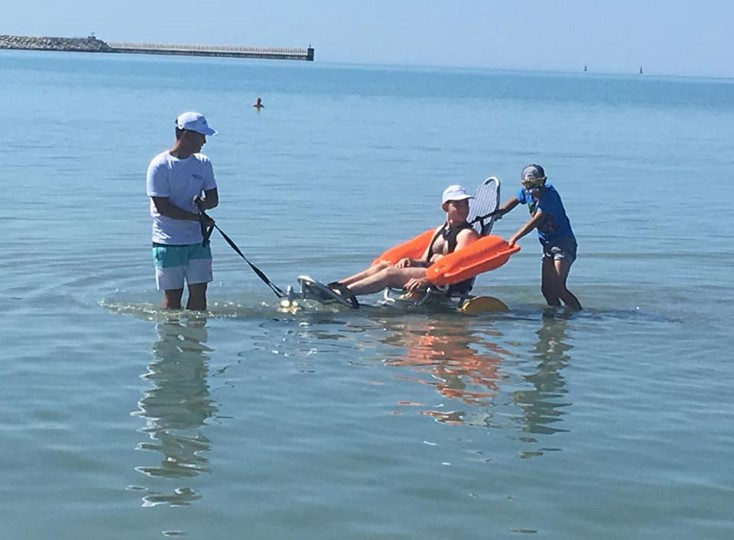 На фото: Каспийское море. Двое волонтеров помогают мальчику купаться на коляска-амфибии