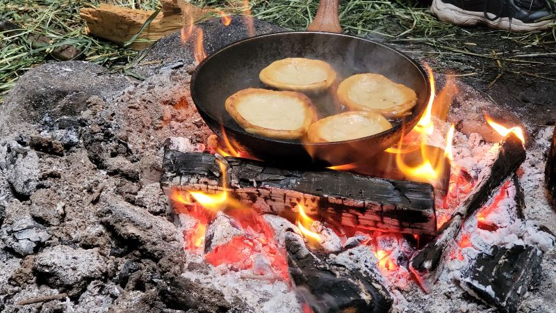 На фото: оладушки жарятся на сковородке на костре