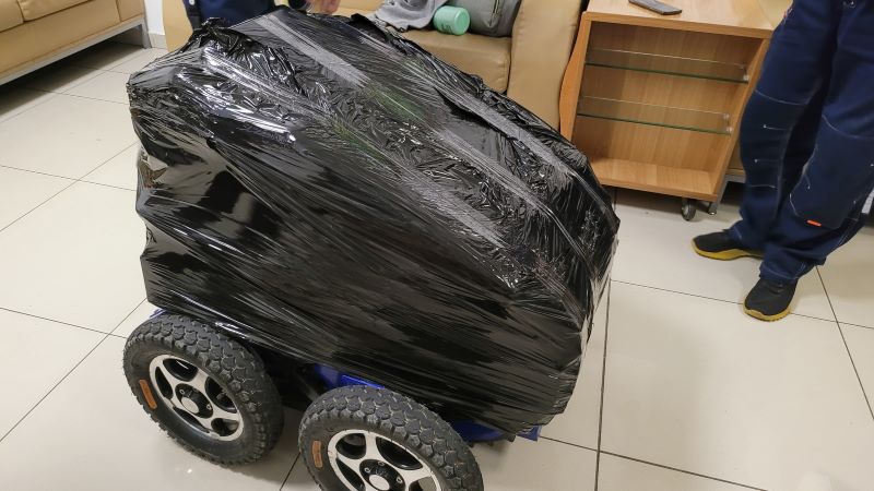 На фото: собранная и обмотанная черным скотчем электроколяска "Катервилл" стоит на полу в аэропорту