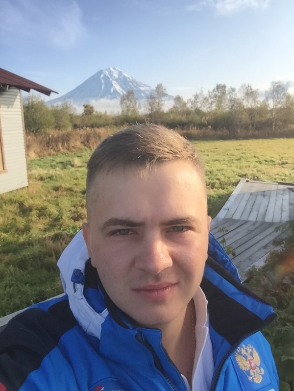 На фото: Максим Попов на турбазе на Камчатке. Позади него на горизонте виден снежный конус вулкана