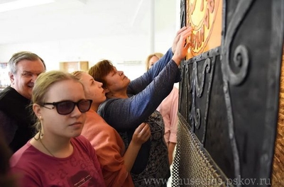 На фото: группа незрячих экскурсантов изучает тактильное панно на стене, экскурсия, музей, Псков