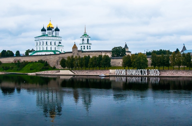 На фото: белоснежный храм с куполами стоит на набережной, река, надпись на берегу большими буквами: "Россия начинается здесь". Псков