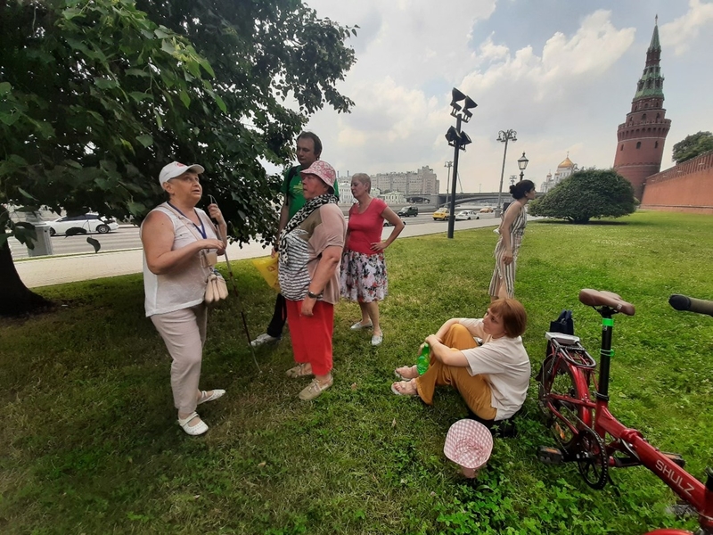 На фото: летний день, Москва, Кремль. Участники инклюзивной экскурсии собрались вокруг экскурсовода на зеленом газоне и слушают рассказ