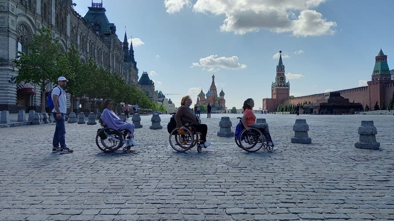 На фото: Красная площадь в Москве. На площади друг за другом выстроились три девушки на инвалидных колясках и молодой человек  - как будто они переходят площадь по брусчатке в стиле обложки альбома группы Битлз "Эбби роуд".  .