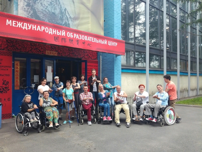 На фото: группа участников инклюзивного ансамбля - люди на инвалидных колясках, перед входом в образовательный центр