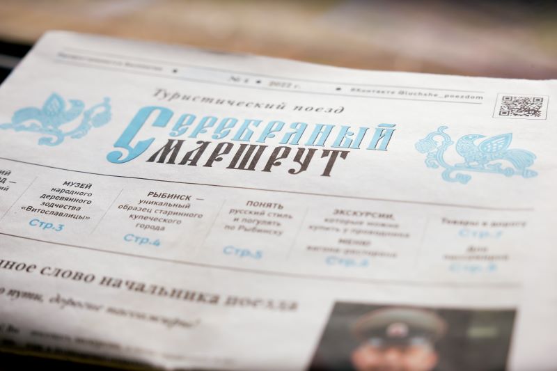 На фото: в купе поезда на столе лежит газета с названием "Серебряный маршрут", рассказывающая о поезде и туристических достопримечательностях в городах