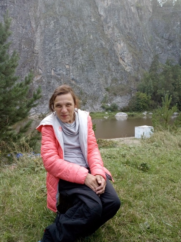 На фото: Елена Лачкова сидит возле реки на траве и улыбается