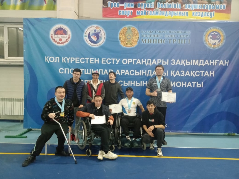 На фото: церемония награждения участников чемпионата. Группа спортсменов с инвалидностью стоит перед большим баннером с названием чемпионата. Спортсмены держат в руках медали и грамоты