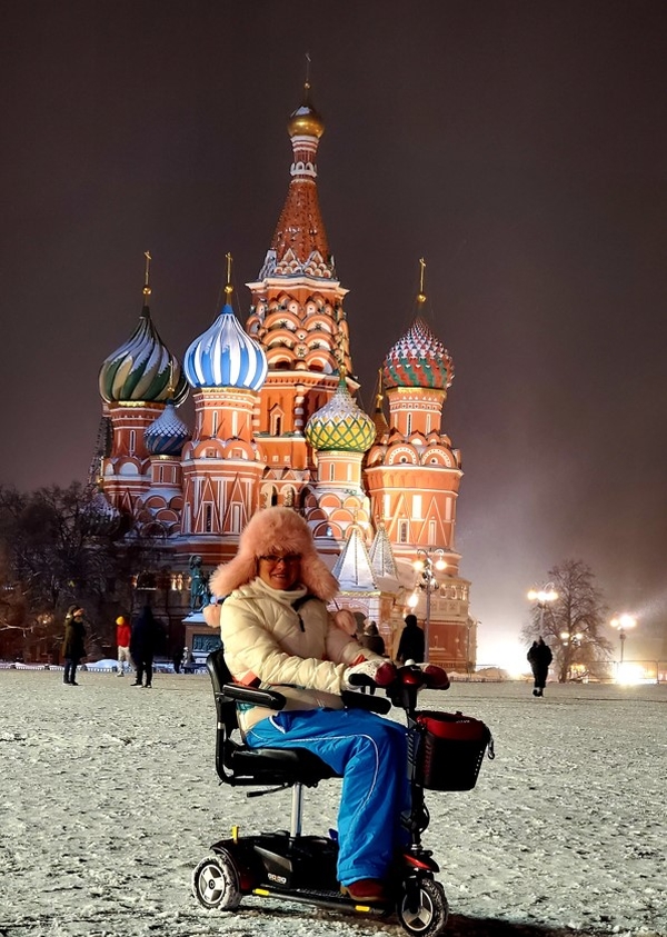 На фото: Юлия Ричардсон в теплом зимнем костюме, пушистой розовой шапке, сидит на мобильном скутере на Красной площади, засыпанной снегом