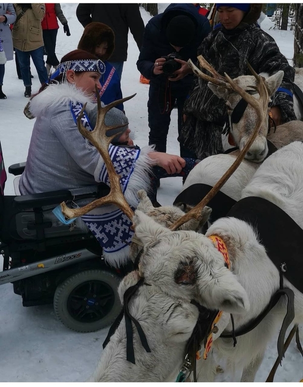 На фото: Ольга Миронова в национальной одежде северных народов на инвалидной коляске держит на руках маленького сына. Рядом с ними стоит упряжка оленей. Ольга м мальчик гладят оленей