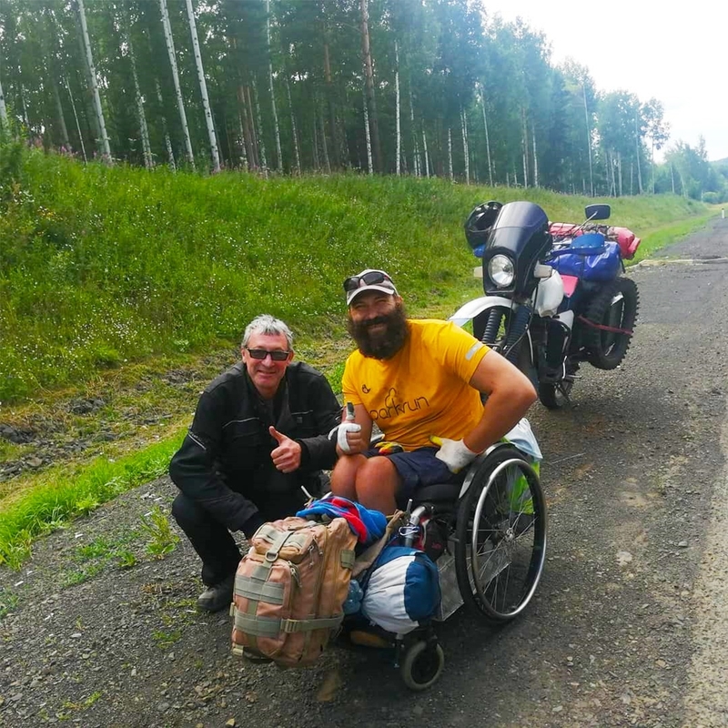 На фото6 дорога на Байкал. Виктор Сибирин на инвалидной коляске с рюкзаком фотографируется рядом с попутчиком -  водителем мотоцикла