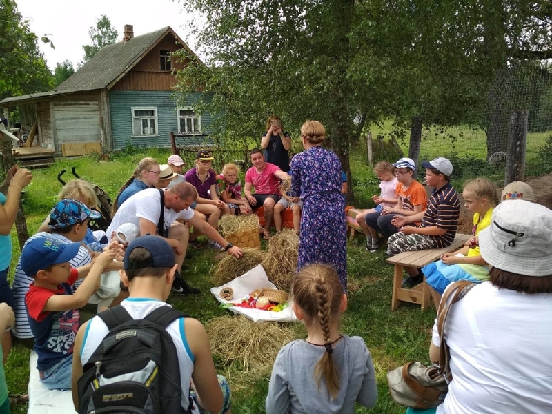 На фото: группа детей сидит кружком на траве вокруг преподавателя на творческом занятии на природе