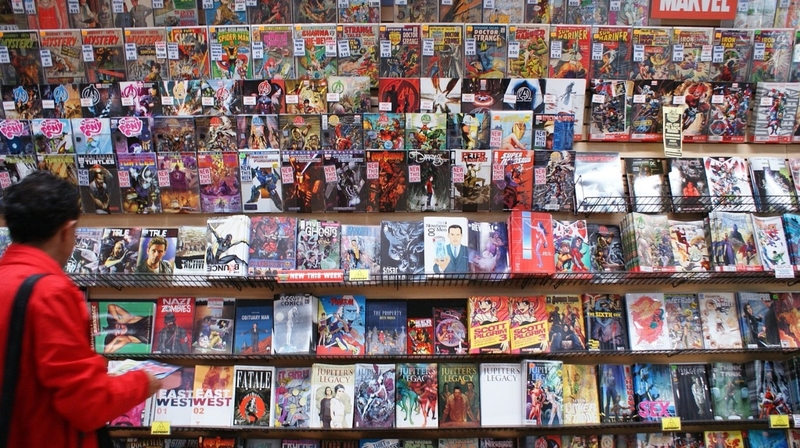 На фото: мужчина в красной куртке перед стеллажами с комиксами в книжном магазине