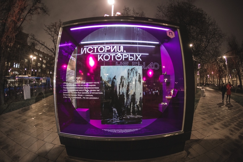 На фото: экспонат выставки в Ильинском сквере - большой стеклянный куб, подсвеченный фиолетовым светом, с экспонатами - предметами участников выставки, фотографиями и цитатой - фрагментом интервью участника на стенке куба