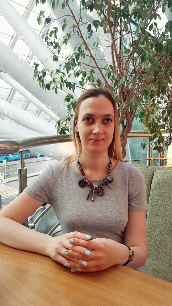 На фото: Евгения Малышко сидит в кафе за столом, положив руки на деревянную столешницу